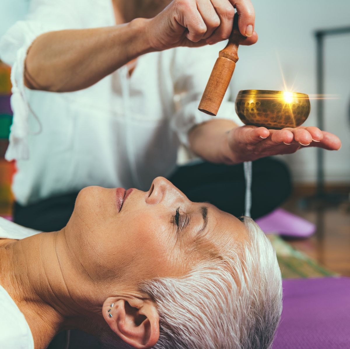 Older woman lying down, listening to a metal singing bowl played in the background