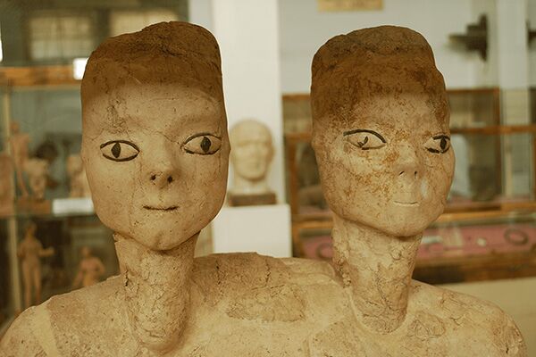 Ain Ghazal statues, two heads perched on long necks, connected to the same torso. The eyes are green from Dioptase