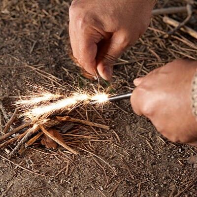 Hands starting a fire by striking steel and flint to create a spark over dry tinder