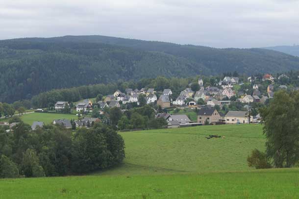 A small town with lots of green grass and forested hills