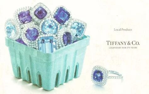 Advertisement by Tiffany & Co showing bright blue and purple tanzanites haloed in diamonds, in a pink box like berries