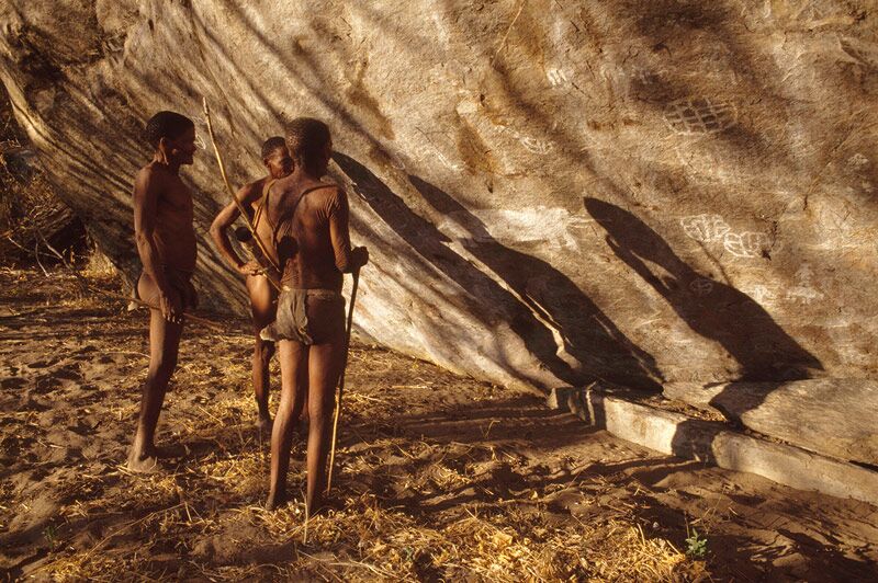 Three San traditional hunter and gather men looking at rock art drawn on Tsodilo Hills Botswana